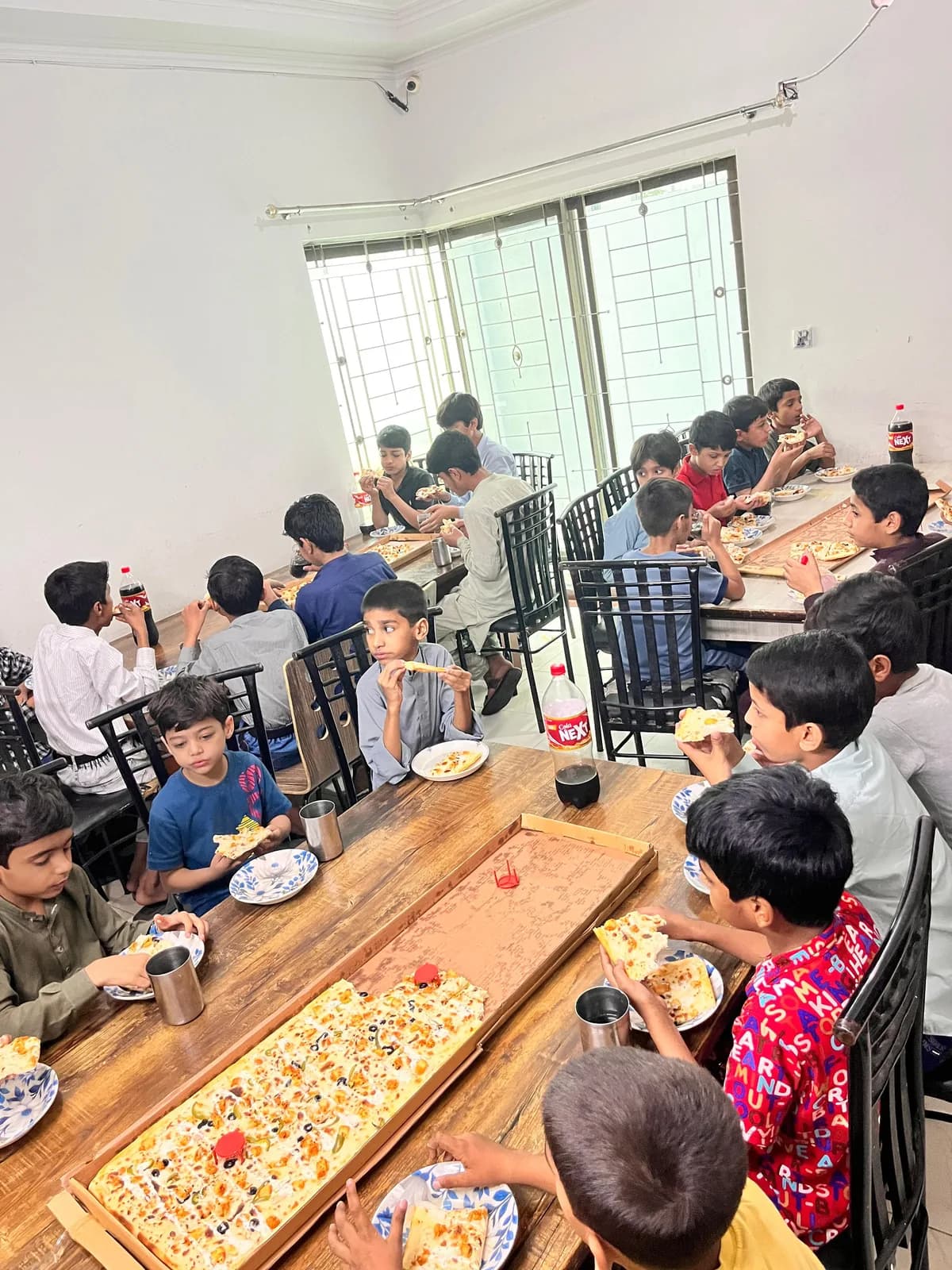 Children at Aman Little Angels Orphanage sharing pizza at a long table during an RFWO distribution drive
